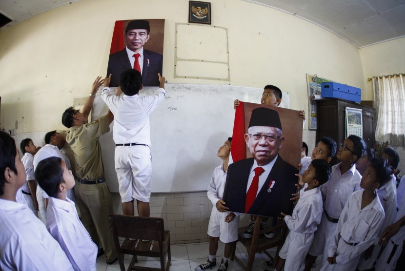 Siswa SD Negeri Joglo Solo dibantu guru memasang foto Presiden Joko Widodo dan dan Wakil Presiden Ma'ruf Amin di ruang kelas sekolahnya di Solo, Jawa Tengah, Senin (21/10/2019). 