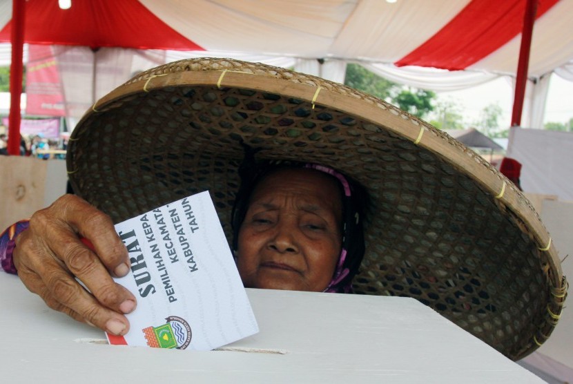 Seorang ibu yang menggunakan topi caping, memasukkan surat suara kedalam kotak saat menggunakan hak pilihnya pada Pemilihan Kepala Desa (Pilkades) serentak Kabupaten Tangerang di Desa Daru, Kabupaten Tangerang, Banten, Minggu (1/12/2019).