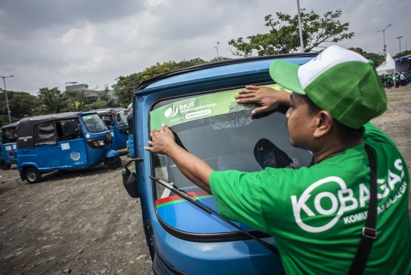 Pengemudi menempel stiker BPJS Ketenagakerjaan ke bajajnya di kawasan Pantai Carnaval Ancol, Jakarta Utara. BPJamsostek menyebut pengelolaan dana milik pekerja selalu diawasi OJK