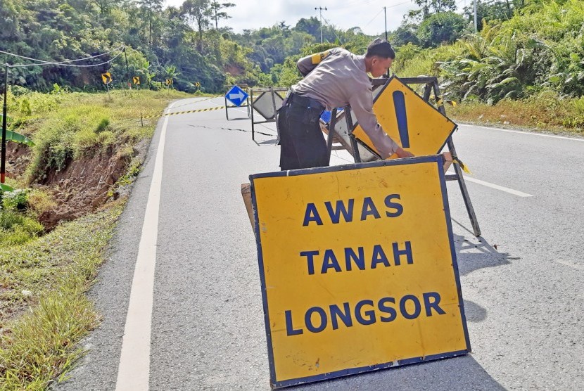 Seorang anggota Polsek Entikong memasang papan peringatan di lokasi jalan lintas negara yang mengalami retak akibat tanah longsor di perbatasan Entikong, Kabupaten Sanggau, Kalimantan Barat, Kamis (26/12/2019). 