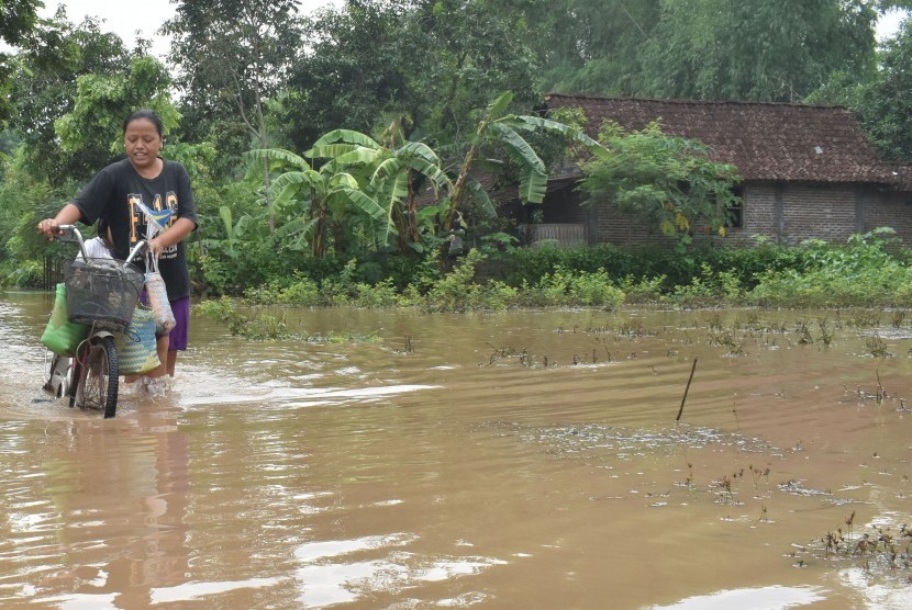 Warga menuntun sepedanya saat melintasi jalan yang terendam banjir di Kabupaten Madiun, Jawa Timur, Sabtu (28/12/2019).