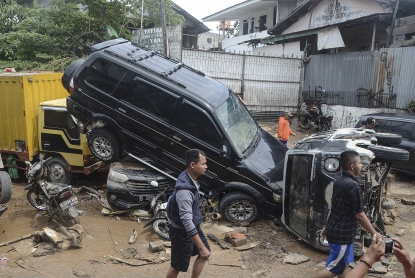 Sejumlah warga berjalan di dekat mobil yang rusak pascabanjir di Perumahan Pondok Gede Permai Bekasi, Jawa Barat, Kamis (2/1/2020). Pembangunan bendungan di Ciawi dan Sukamahi disebut bisa membantu atasi banjir Jabodetabek.