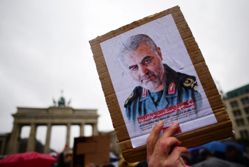 Seorang pemrotes memegang sebuah kardus yang memperlihatkan potret Letnan Jenderal Komandan Revolusioner Iran (IRGC) dan komandan Pasukan Quds Qassem Soleimani selama demonstrasi di depan Gerbang Brandenburg, dekat dengan kedutaan AS di Berlin, Jerman, 4 Januari 2020. Amerika Serikat telah mendeteksi pasukan rudal Iran pada kondisi siaga tinggi pascatewasnya Soleimani. 