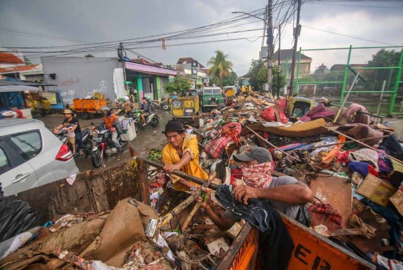 Petugas memindahkan sampah yang menumpuk di sisi jalan pascabanjir 