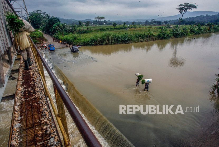 Warga melintasi jalan yang tergenang luapan air Sungai Cileungsi.