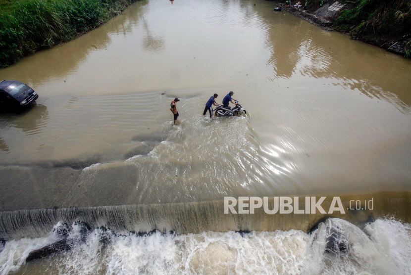 Pengendara roda dua memaksakan untuk melintasi jalan yang tergenang luapan air Sungai Cileungsi di Jalan alternatif Desa Gunung Sari, Citeureup, Kabupaten Bogor, Jawa Barat.
