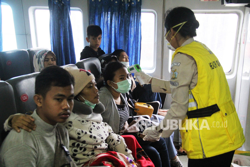 Seorang Petugas medis (kanan) memeriksa suhu tubuh penumpang menggunakan thermometer non kontak di dalam kapal yang baru tiba dari Melaka, di Pelabuhan PT Pelindo I Dumai di Dumai, Riau, Sabtu (01/2/2020).