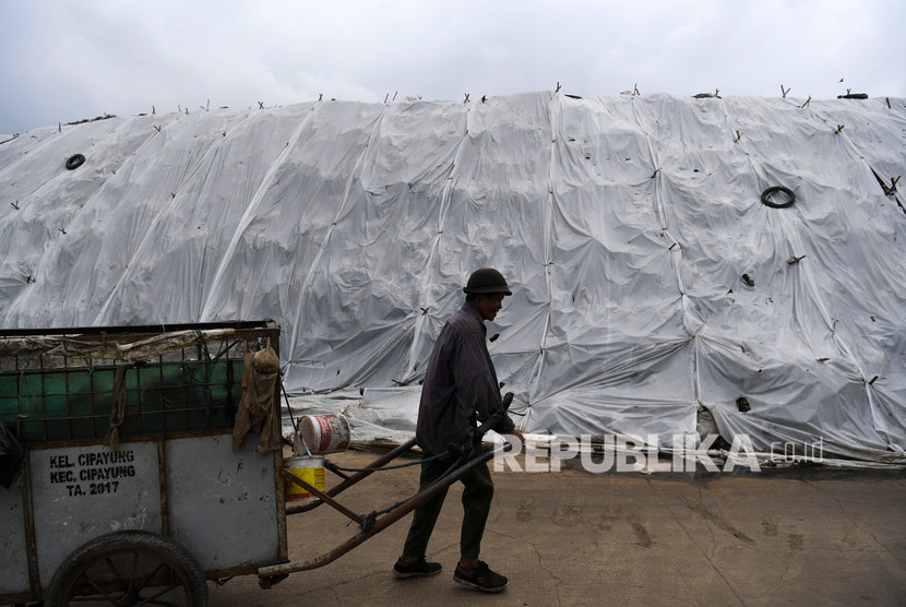 Pekerja membawa sampah menggunakan gerobak melintasi plastik yang menutup tumpukan sampah di TPA Cipayung, Depok, Jawa Barat, Jumat (6/2/2020).