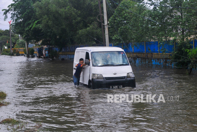 Pengendara mendorong mobilnya yang mogok karena menerobos banjir di Pulogadung, Jakarta Timur, Ahad (23/2/2020).