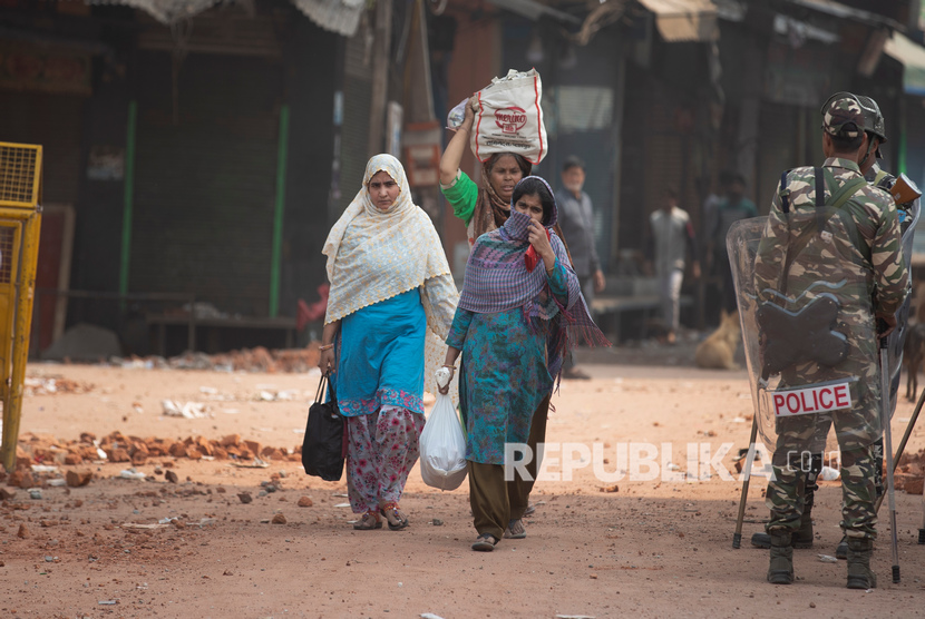 Wanita berjalan melewati tentara Paramiliter India yang berjaga-jaga di daerah yang menyaksikan kekerasan pada hari Selasa di New Delhi, India, Rabu, 26 Februari 2020.(AP/Rajesh Kumar Singh)