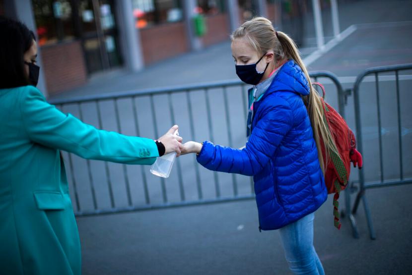 Seorang guru memberikan hand sanitizer kepada siswanya sebelum masuk ke dalam sekolah di Brussels, Senin (18/5).