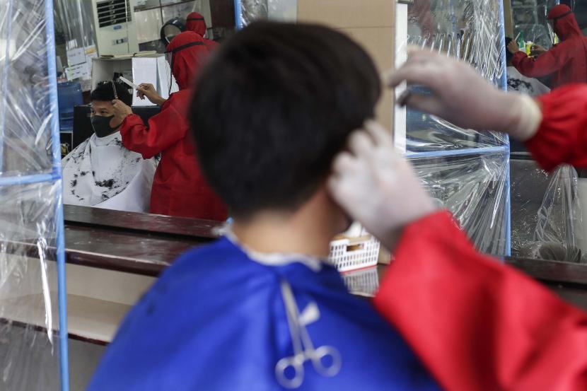 Seorang tukang cukur dengan mengenakan pakaian pelindung memotong rambut di sebuah tempat pangkas rambut (ilustrasi) 