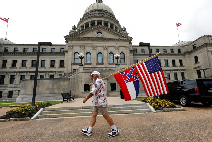 Seorang warga membawa bendera Mississippi dan bendera Amerika Serikat di Jackson, Mississippi, Sabtu (27/6). Politisi-politisi di Negara Bagian Mississippi, Amerika Serikat (AS) sepakat untuk menghapus lambang Konfederasi di bendera negara bagian. 