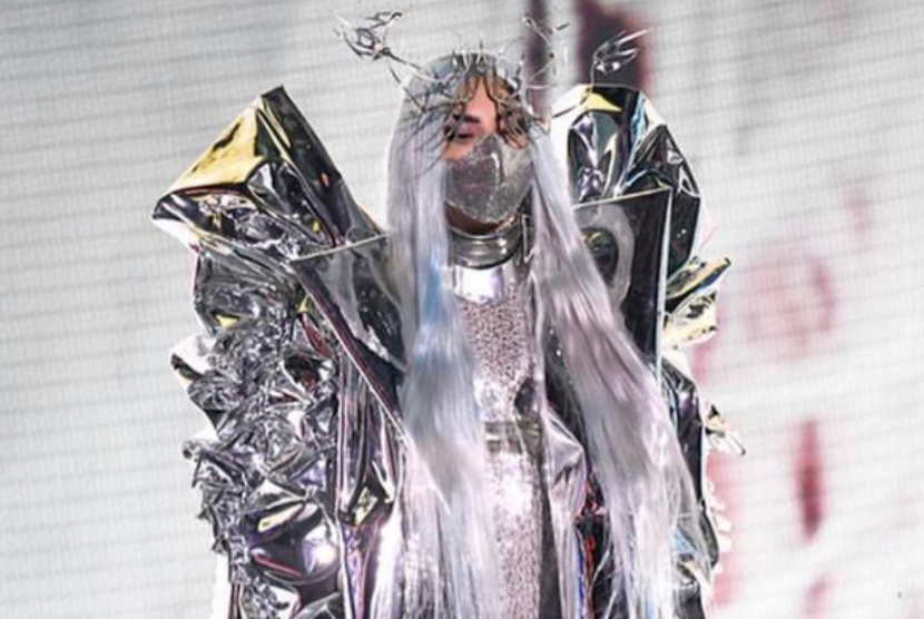 Lady Gaga mengenakan masker perak mengkilap karya desainer Indonesia pemilik jenama Maison Met, Mety Choa. Gaga pernah mengalami masalah kesehatan mental di awal ketenarannya.
