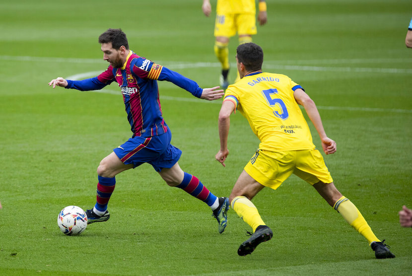 Pemain Barcelona Lionel Messi (kiri) melewati pemain Cadiz dalam pertandingan Liga Spanyol antara FC Barcelona dan Cadiz di Stadion Camp Nou, Barcelona, Spanyol, Ahad (21/2).