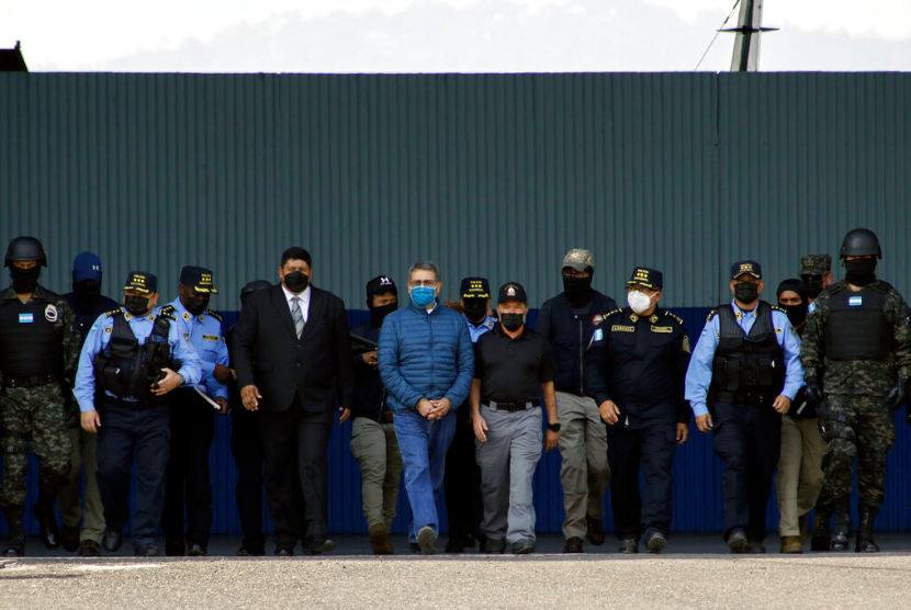 Mantan Presiden Honduras Juan Orlando Hernandez, tengah, mengenakan masker pelindung biru dan diborgol, dikawal dengan pengawalan ketat menuju pesawat yang menunggu di pangkalan Angkatan Udara di Tegucigalpa, Honduras, Kamis, 21 April 2022. Honduras mengekstradisi Hernandez ke Amerika Serikat.