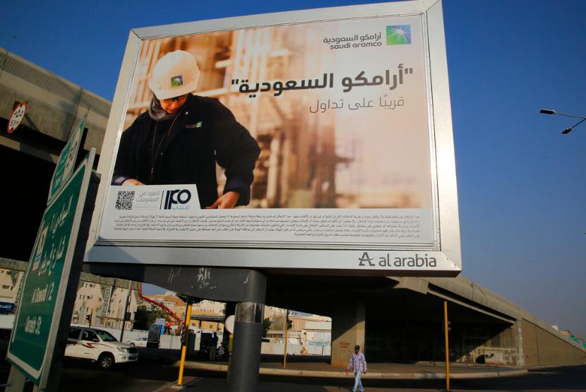 Seorang pria berjalan di bawah papan reklame yang menampilkan iklan raksasa minyak milik negara Arab Saudi Aramco dengan tulisan Arab 