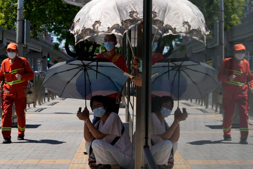 Warga menutupi dari matahari dengan payung saat mereka menunggu bus, Jumat, 15 Juli 2022, di Beijing. Suhu telah melampaui rekor sepanjang masa ketika gelombang panas menyapu sebagian besar negara.