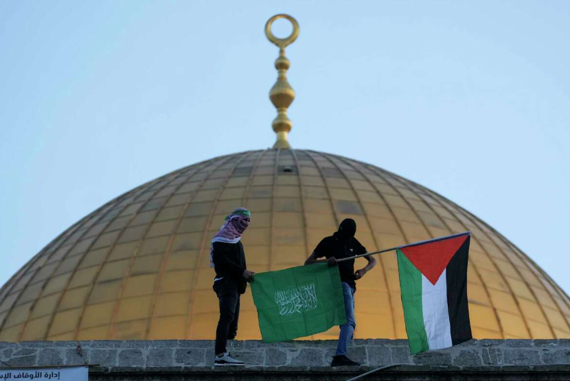 Warga Palestina bertopeng membawa bendera Palestina dan Hamas saat perayaan Idul Fitri di sebelah Masjid Kubah Batu di kompleks Masjid Al-Aqsa di Kota Tua Yerusalem, 2 Mei 2022. Kelompok militan Palestina Hamas mengancam tindakan bermusuhan terhadap Israel atas apa yang disebutnya 