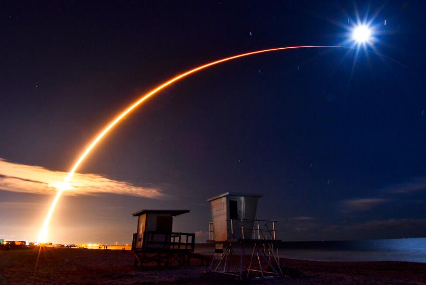 Roket SpaceX Falcom 9 terlihat melengkung di langit menuju bulan yang memudar, dilihat dari Shepard Park di Cocoa Beach, Florida, Sabtu, 15 Oktober 2022, setelah diluncurkan dari Launch Complex 40 di Cape Canaveral Space Force Station.