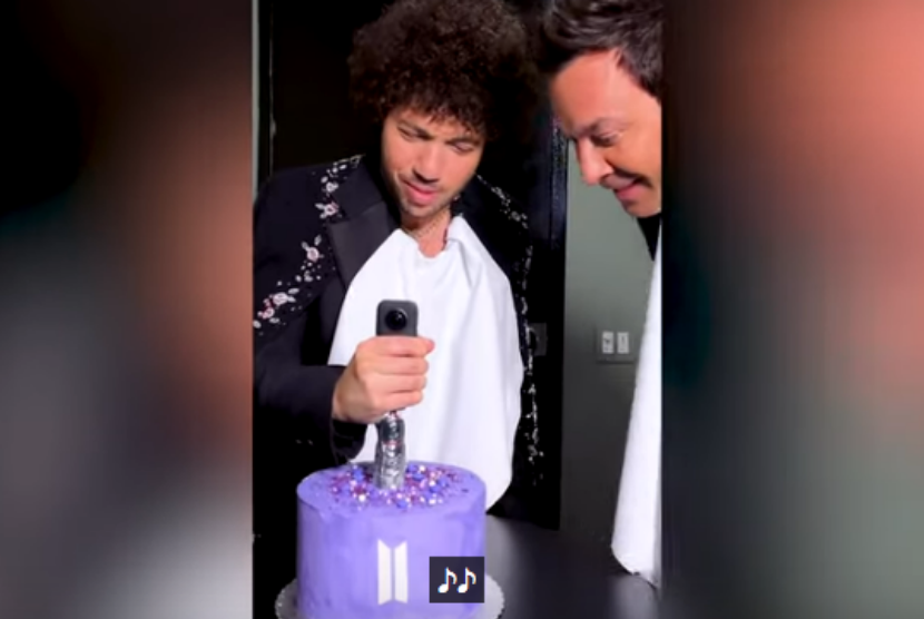 Musisi Benny Blanco (kiri) menancapkan kamera 360 ke kue berlogo BTS disaksikan pembawa acara The Tonight Show, Jimmy Fallon.