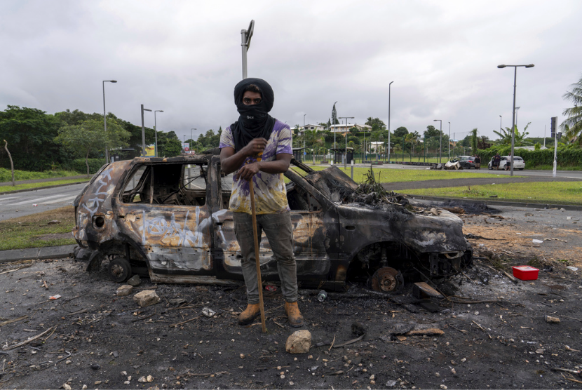 Seorang pria berdiri di depan mobil yang terbakar setelah kerusuhan di Noumea, Kaledonia Baru, Rabu, 15 Mei 2024.