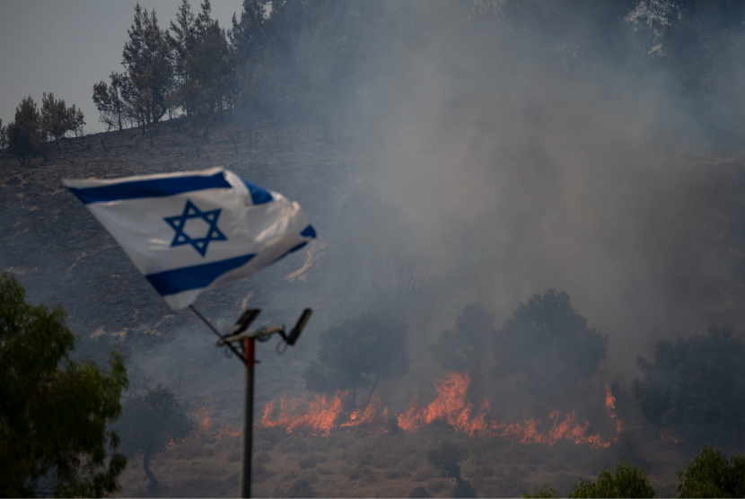 Bendera Israel berkibar di samping api yang berkobar akibat rudal Hizbullah di kawasan dekat perbatasan dengan Lebanon, Israel utara di Safed, Rabu, 12 Juni 2024.