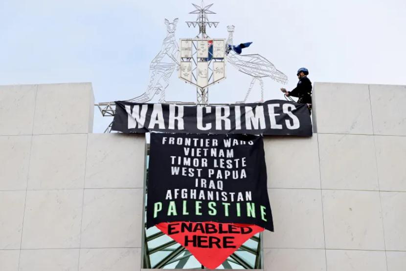 Seorang petugas Polisi Federal Australia mencopot spanduk pro-Palestina yang digantung di Gedung Parlemen Australia di Canberra pada Kamis (4/7/2024).