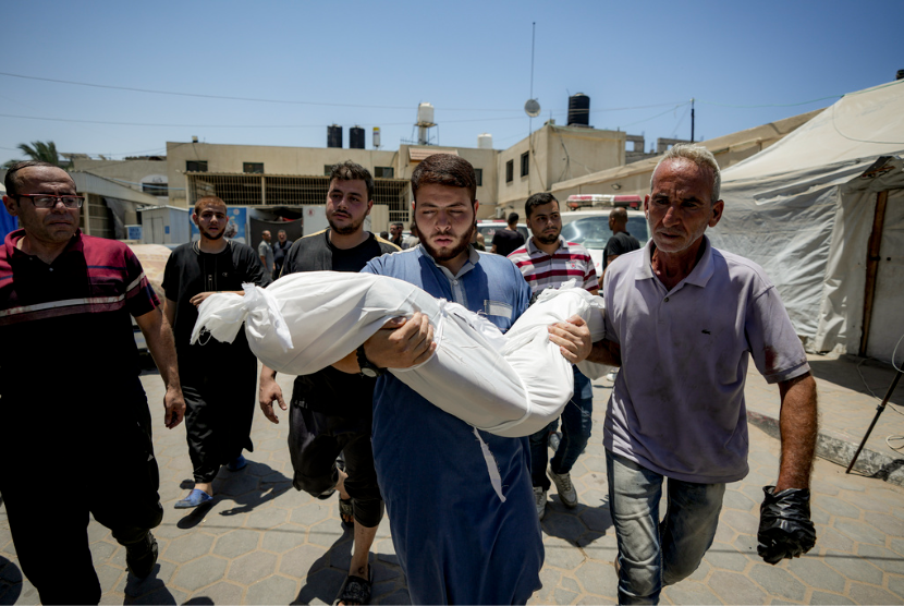 Seorang pria Palestina memegang jenazah anak yang syahid dalam pemboman Israel di Jalur Gaza, di kamar mayat rumah sakit di Deir al-Balah, Selasa, 9 Juli 2024.