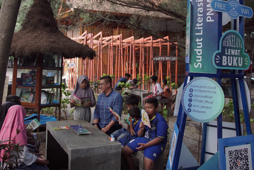 Sekretaris Perusahaan PNM, L Dodot Patria Ary menyimak bacaan salah seorang anak di Pusat Literasi PNM, Pantai Bangsring, Banyuwangi, Kamis (26/9/2024).