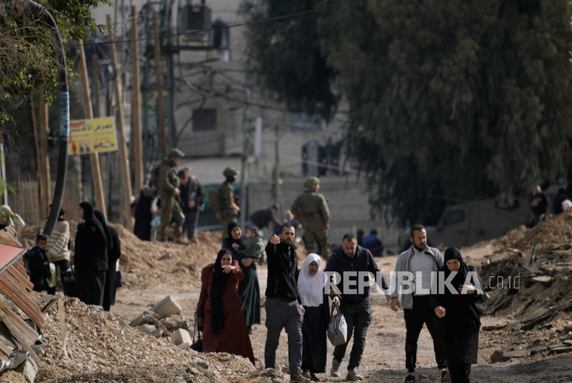 Tentara Israel berjalan di depan warga Palestina yang mengungsi akibat operasi militer Israel dari kamp pengungsi Jenin di Tepi Barat, Kamis, 23 Januari 2025.