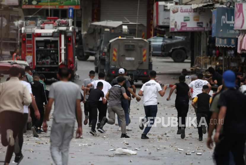 Warga Palestina melemparkan batu ke kendaraan militer Israel saat bentrokan usai serangan tentara Israel di kota Nablus, Tepi Barat, 4 Mei 2025.