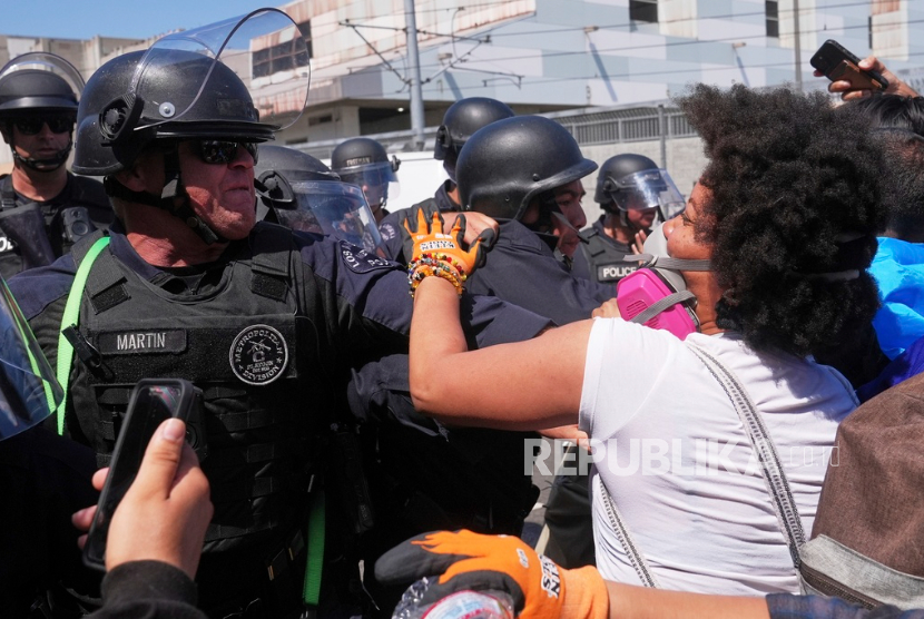 Para pengunjuk rasa menghadapi barisan polisi di pusat kota Los Angeles, Ahad, 8 Juni 2025, menyusul protes penggerebekan imigrasi.