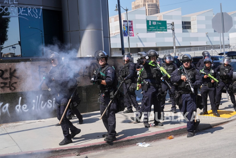 Para pengunjuk rasa menghadapi barisan polisi di pusat kota Los Angeles, Ahad, 8 Juni 2025, menyusul protes penggerebekan imigrasi.