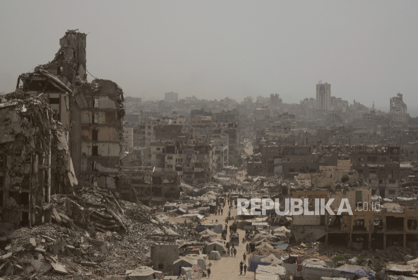 Orang-orang berjalan di jalan yang dikelilingi gedung-gedung yang hancur akibat bombardir Israel di Jalur Gaza, Selasa, 29 Juli 2025.