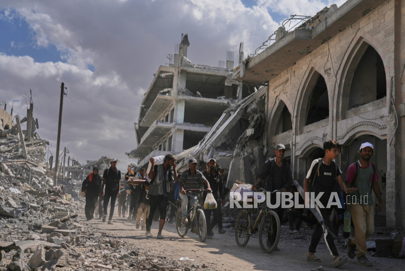 Pengungsi Palestina berjalan melewati bangunan yang hancur saat mereka kembali ke rumah mereka di Khan Younis, Jalur Gaza selatan, Jumat, 10 Oktober 2025.