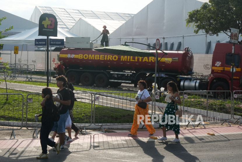 Orang-orang berjalan melewati petugas pemadam kebakaran yang sedang bekerja di KTT Iklim PBB COP30 setelah kebakaran, Kamis, 20 November 2025, di Belem, Brasil.