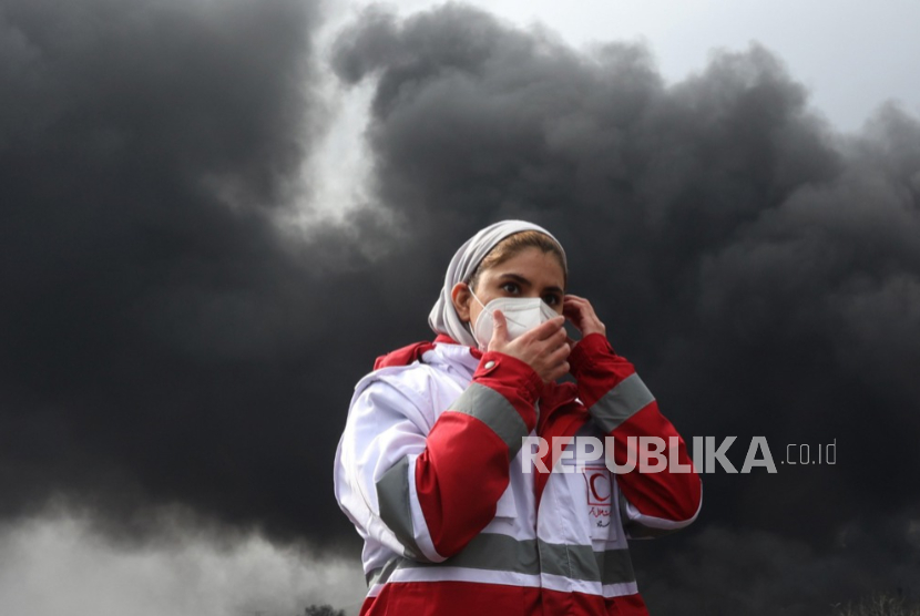 Seorang anggota Bulan Sabit Merah Iran berjalan ketika asap masih mengepul dari Kilang Minyak Shahran menyusul serangan udara tadi malam di Teheran, Iran, 8 Maret 2026.