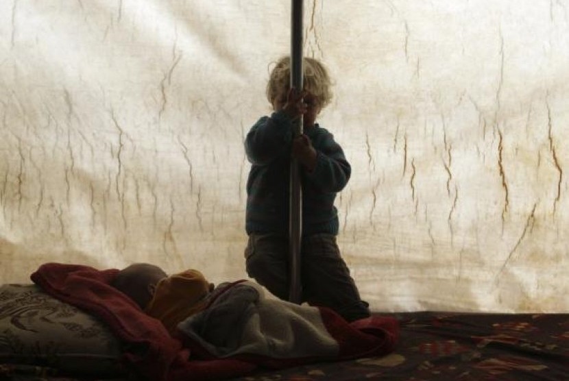 A child hides his face as he sits inside a tent at the Jarjanaz refugee camp in the southern countryside of Idlib November 30, 2014.