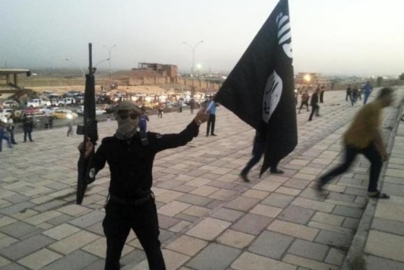 A fighter of the Islamic State of Iraq and the Syria (ISIS) holds an ISIS flag and a weapon on a street in the city of Mosul, June 23, 2014.