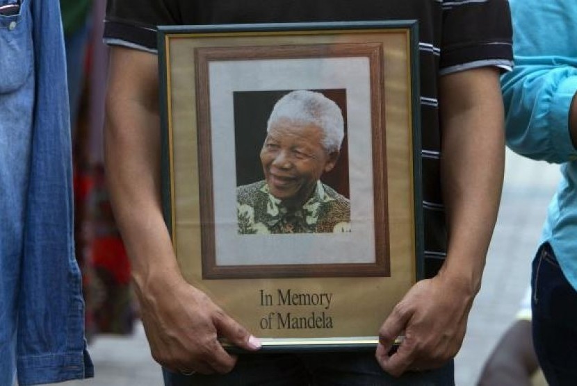 A man holds a tribute photograph as he watches the funeral service for former South African President Nelson Mandela on a large screen television in Cape Town, December 15, 2013.