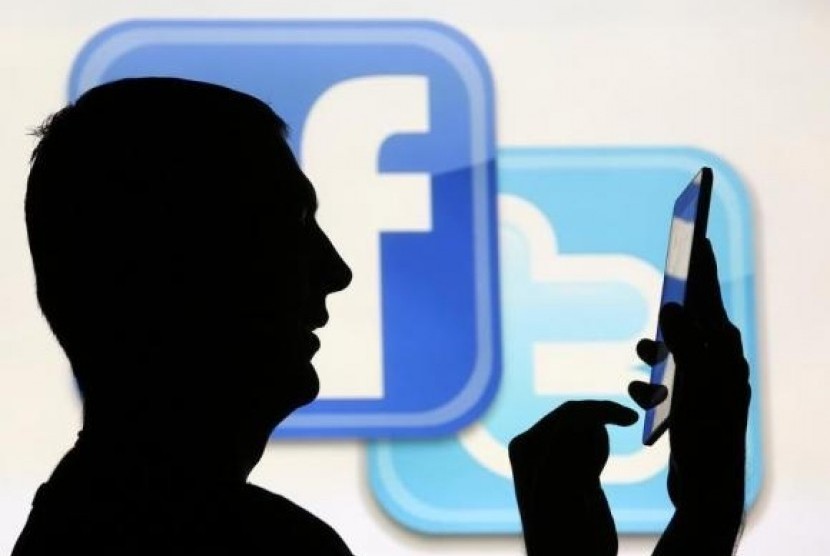 A man is silhouetted in front of a video screen with the Facebook and Twitter logos. (illustration)