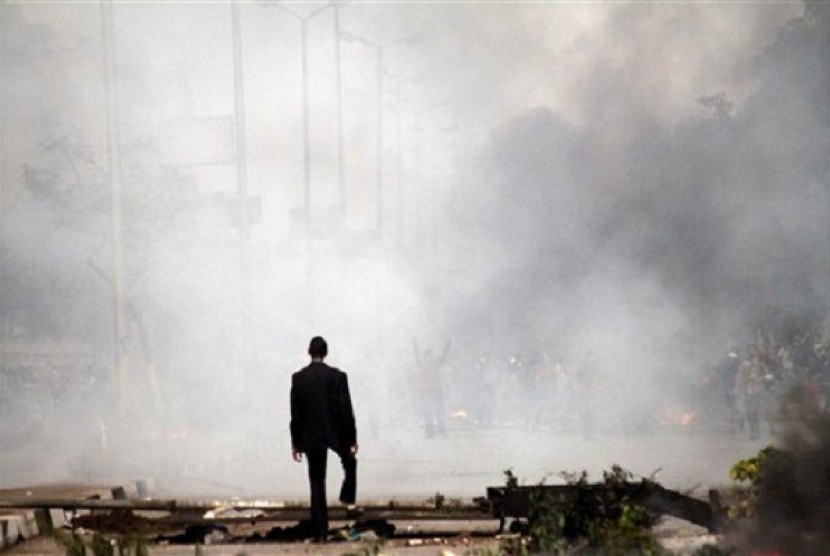 A man stands amid the smoke from tear gas fired by Egyptian riot police in Cairo, Egypt, Friday, Nov. 29, 2013, to disperse hundreds of demonstrators.