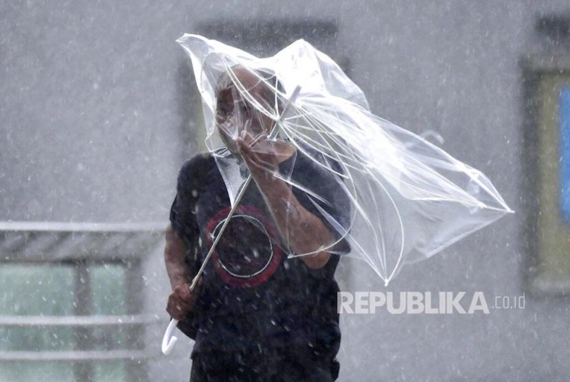 Seorang warga berusaha mengembangkan payungnya di tengah hembusan angin kencang akibat topan Faxai di Tokyo, Senin (9/9).