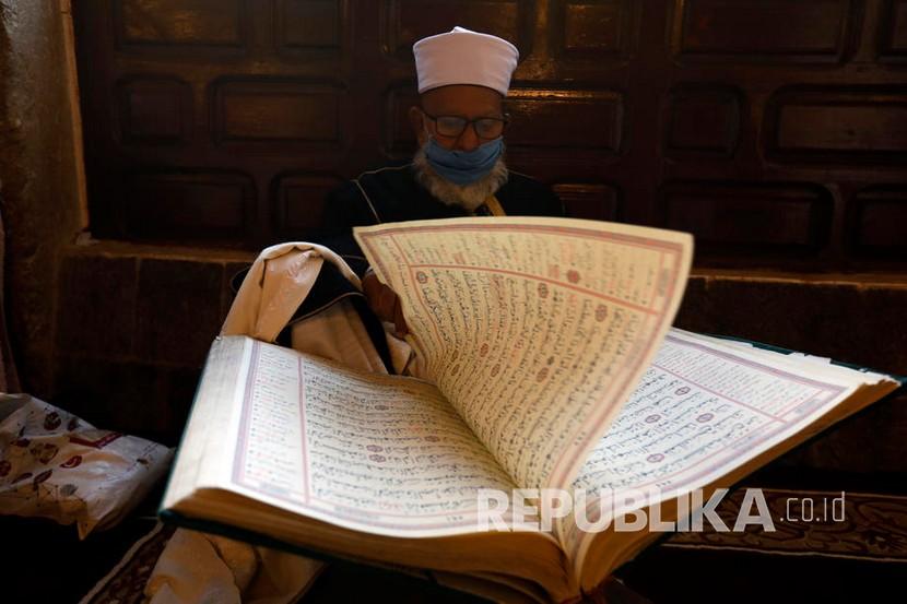  Ibnu Katsir dan Empat Tahap Memahami Alquran. Seorang pria mengenakan masker membaca Alquran di sebuah masjid Ibu Kota Sanaa, Yaman.