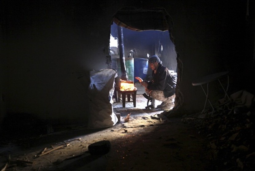 A member of opposition group warms himself around a fire as he is seen through a wall opening in Deir al-Zor, eastern Syria, December 12, 2013. (illustration)
