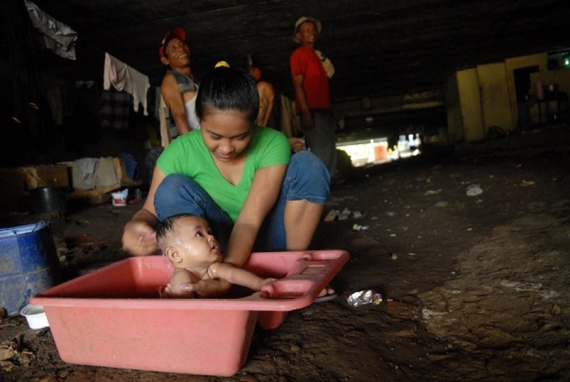 A mother baths her baby in a slum area located under the bridge, where her family live. Uneven wealth distribution in this country still pose a major problem to eradicate poverty. (illustration) 