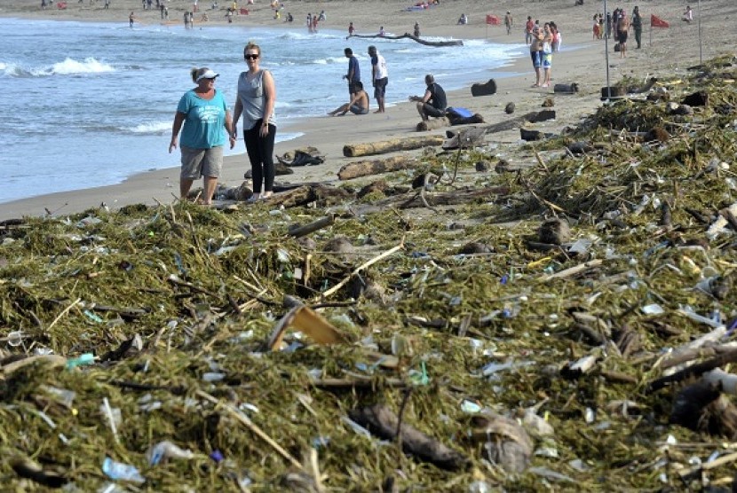 A number of foreign tourits walk near a stack of garbage at Kuta Beach, Bali.  