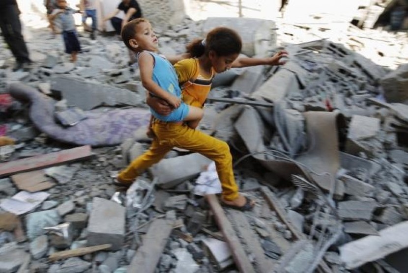 A Palestinian girl carries a child across rubble from a building that police said was destroyed by an Israeli air strike, in the Burij refugee camp in the central Gaza Strip August 1, 2014.