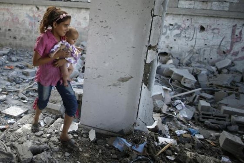 A Palestinian girl holding her sister walks through debris near remains of a mosque, which witnesses said was hit by an Israeli air strike, in Beit Hanoun in the northern Gaza Strip August 25, 2014.